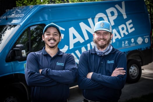 Two lawn technicians smiling and standing in front of truck
